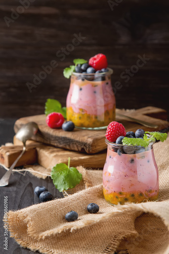 Fresh homemade yogurt in a glass jar with blueberries, raspberries, mint and Passionfruit. On a wooden board, metal vintage spoon. Dark background.