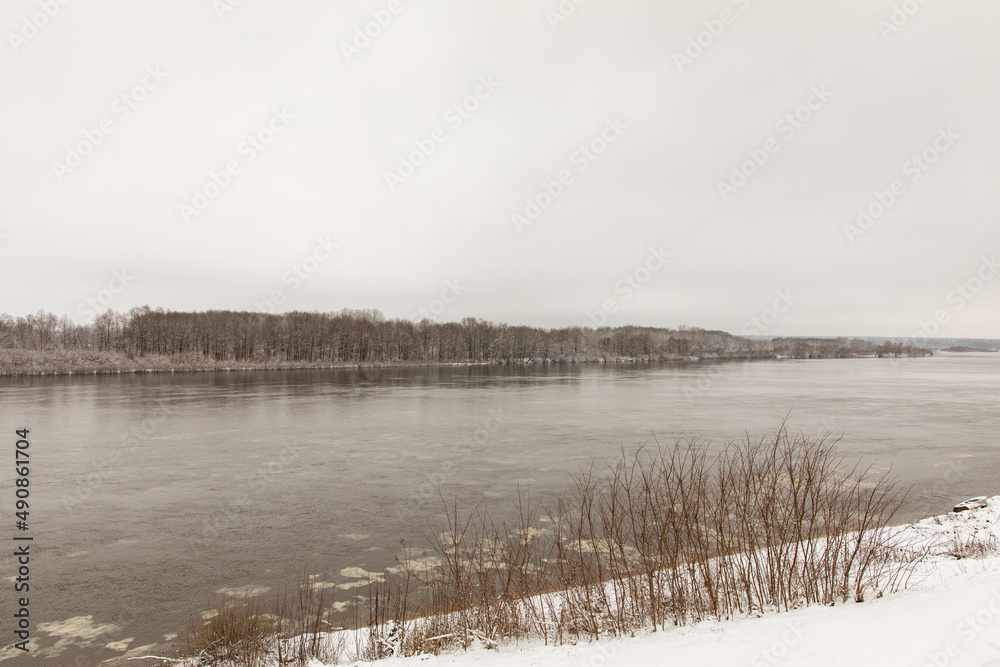 Fototapeta premium A river in spring or winter with unfrozen water. There are trees in the snow on the shore.