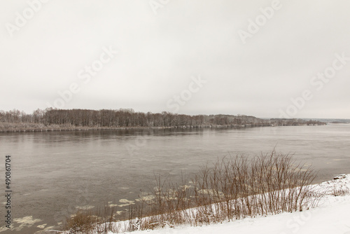 A river in spring or winter with unfrozen water. There are trees in the snow on the shore.