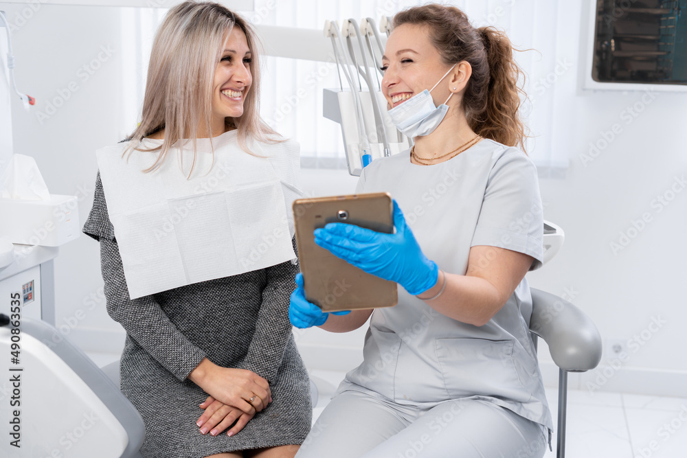 Dentist and patient choose treatment in consultation with medical equipment in the background. smiling woman dentist explaining x-ray of teeth to patient in dentist office. Dentist and patient choose treatment in consultation with medical equipment in the background. smiling woman dentist explaining x-ray of teeth to patient in dentist office.