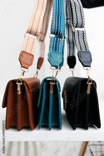 Several multicolored handbags stand on a table against a white background. Handbags view from the side. fashionable women's leather clutch bag. Traditional women's clutch bag with gold hardware and fa