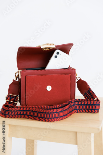 A white phone sticking out of a small purse. small red purse. Phone sticking out of pocket of leather handbag. Isolated on a white background. 