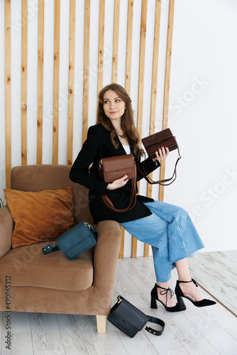 Portrait of a young blonde girl in a jacket and jeans, holding a handbag. fashionable women's leather clutch bag. Traditional women's clutch bag with gold hardware. Fine coloured leather handbag. 