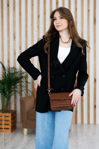 Portrait of a young blonde girl in a jacket and jeans, holding a handbag. fashionable women's leather clutch bag. Traditional women's clutch bag with gold hardware. Fine coloured leather handbag. 