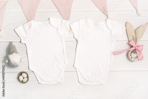 Two white baby bodysuit mockup with Easter decor on white wood background. Easter eggs and gnome with rabbit ears