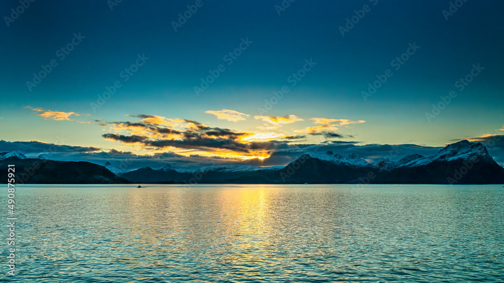 vom Sonnenaufgang orange gefärbte Wolken über den frisch verschneiten Bergen an der Küste von Norwegen, zwischen Nesna und Ørnes im Nordland. blauer Himmel mit bunten Wolken