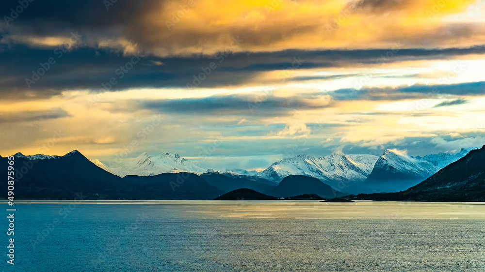 Vom Sonnenaufgang orange gefärbte Wolken über den frisch verschneiten Bergen der Küste von Norwegen, zwischen Nesna und Ørnes im Nordland. 