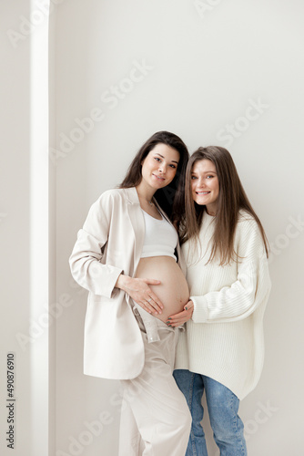 Stylish pregnant brunette girl with beige trouser suit and her friend 
