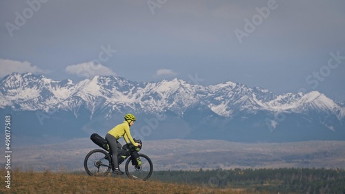 The woman travel on mixed terrain cycle touring with bikepacking. The traveler journey with bicycle bags. Sport tourism bikepacking, bike, sportswear in green black colors. Mountain snow capped. photo