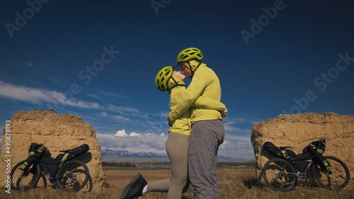 The man and woman travel on mixed terrain cycle bike touring with bikepacking. The two people journey with bicycle bags. Sport sportswear in green black colors. Mountain snow capped, stone arch. photo