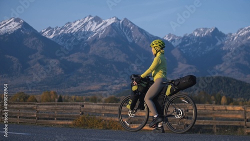 The woman travel on mixed terrain cycle touring with bikepacking. The traveler journey with bicycle bags. Sport tourism bikepacking, bike, sportswear in green black colors. Mountain snow capped.