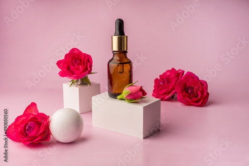 Glass bottle for drops and liquid and oils. Advertising of a cosmetology product. Roses. Pink water. OilFor Face and Body photo