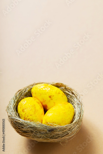 Fototapeta Naklejka Na Ścianę i Meble -  Yellow easter eggs in nest on a beige background. Minimal Easter concept. Top view. Copy space