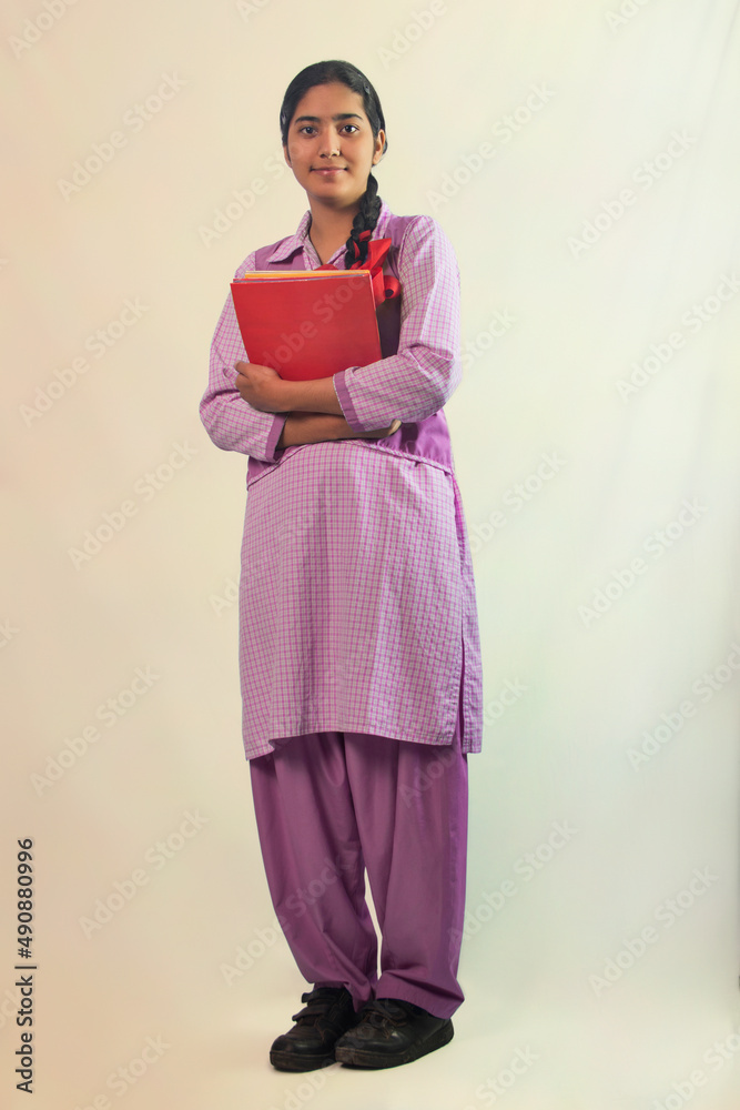 Fototapeta premium A school girl looking at camera with smile while holding book