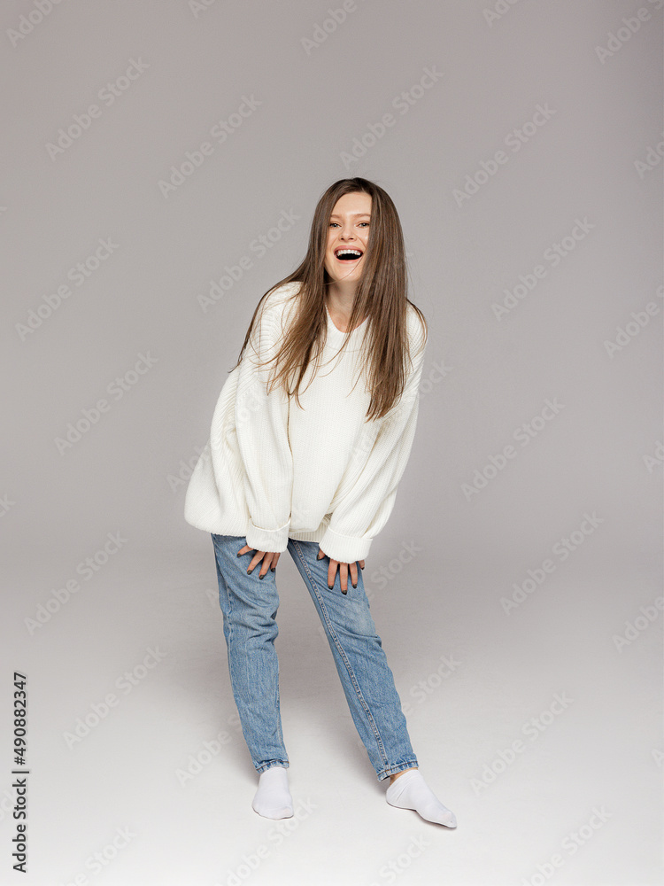 Girl in light jeans and a white oversized sweater on a gray background Girl in light jeans and a white oversized sweater on a gray background