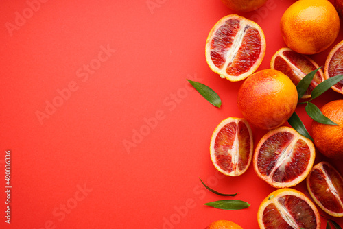 Blood oranges sliced and whole with sprigs of green leaves on a red background, space for tex, top view.