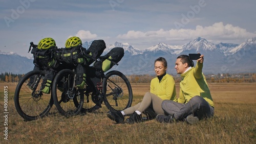 The man and woman travel on mixed terrain cycle touring with bikepacking. The two people journey with bicycle bags. Sport bikepacking, bike, sportswear in green black colors. Mountain snow capped. photo