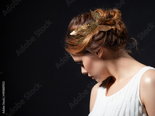 A beautiful ancient goddess from the era of the heroes of Hellas. A young woman in a white tunic and a laurel wreath, an ancient Greek muse or heroine, close-up on a contrasting black background