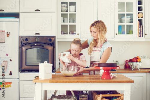 Mixing up the ingredients together. Cute little girl baking in the kitchen at home with her mom.