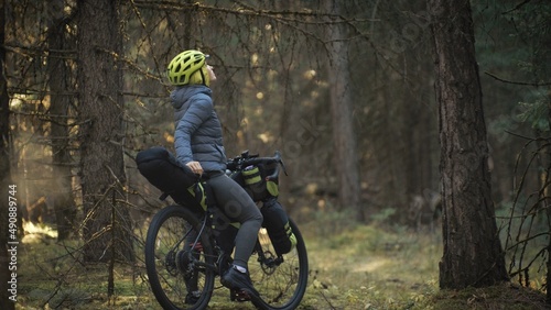The woman travel on mixed terrain cycle touring with bike bikepacking outdoor. The traveler journey with bicycle bags. Stylish bikepacking, bike, sportswear in green black colors. Magic forest park.