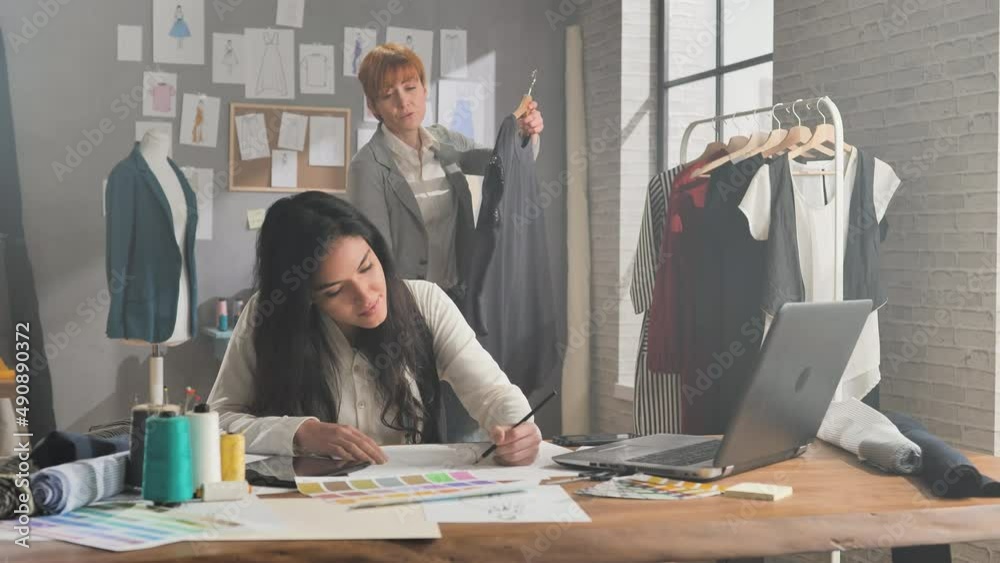 latin hispanic female fashion designer works in studio drawing clothing sketches collection in workshop,two stylist woman small business owner working together in atelier workplace