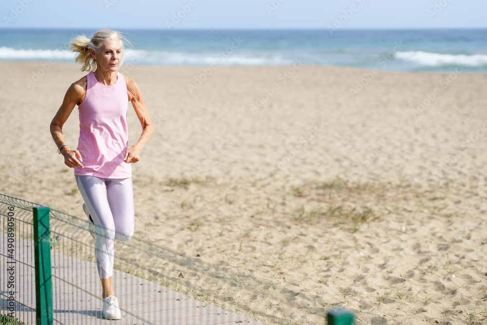 Older female doing sport to keep fit. Mature woman running along the shore of the beach. Older female doing sport to keep fit. Mature woman running along the shore of the beach.