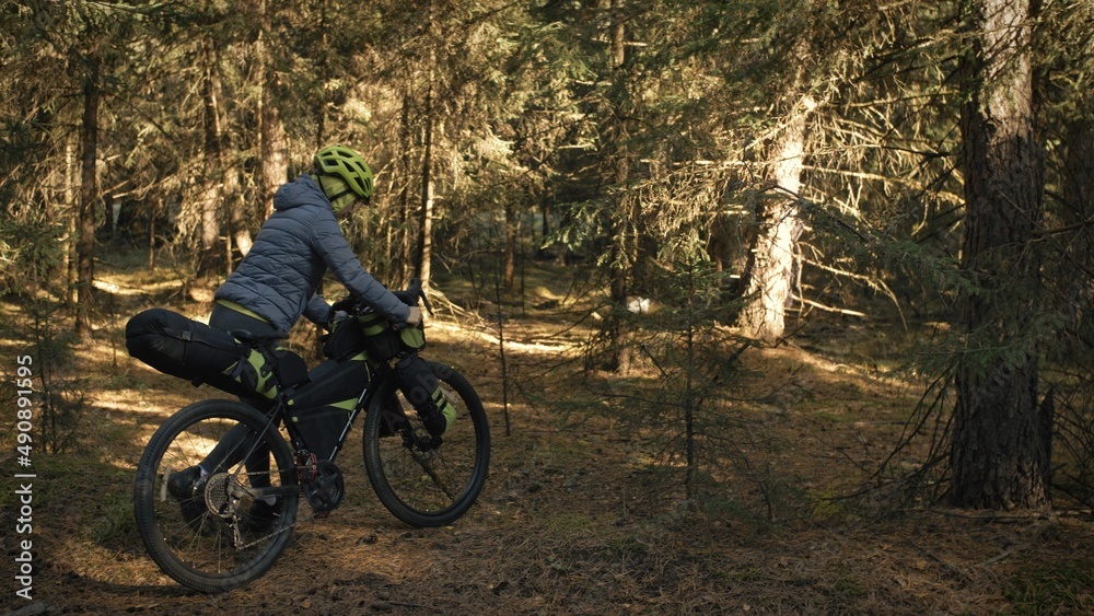 The woman travel on mixed terrain cycle touring with bike bikepacking outdoor. The traveler journey with bicycle bags. Stylish bikepacking, bike, sportswear in green black colors. Magic forest park. The woman travel on mixed terrain cycle touring with bike bikepacking outdoor. The traveler journey with bicycle bags. Stylish bikepacking, bike, sportswear in green black colors. Magic forest park.