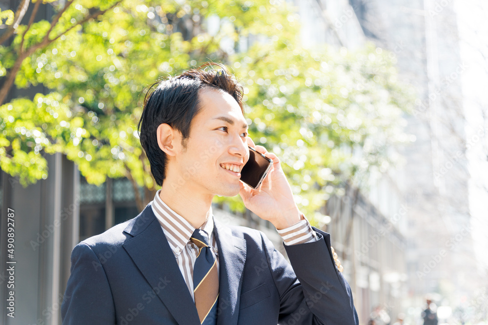 新緑のオフィス街でスマートフォンを使うビジネスマン 新緑のオフィス街でスマートフォンを使うビジネスマン