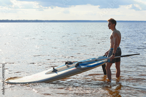 Young fit active person with stand up paddle board and oar goes in water to exercise. Sup surfing in summer