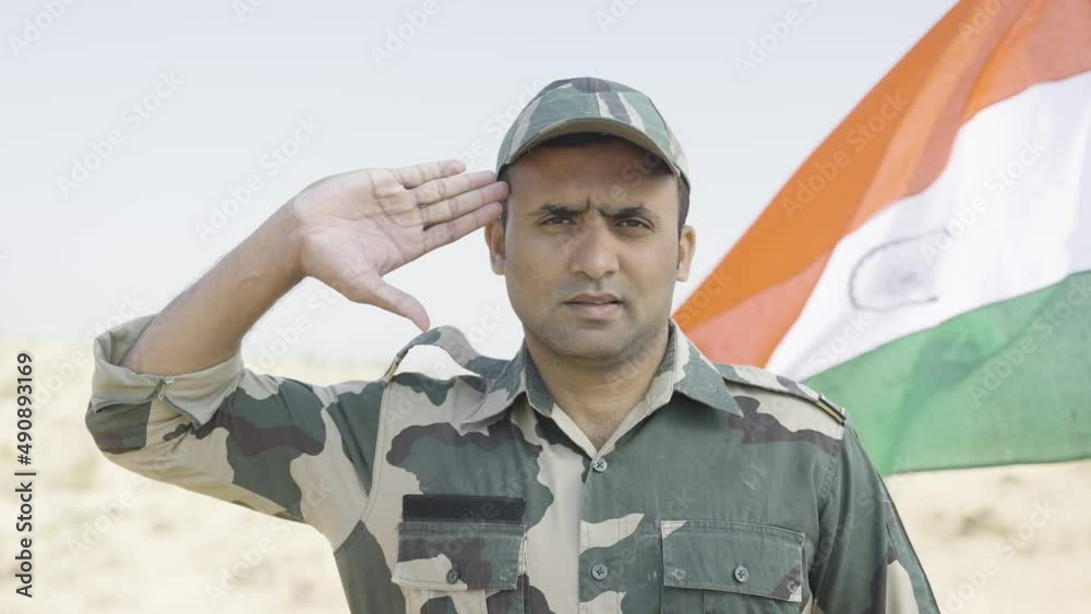 army officer saluting by looking at camera in front of waving Indian flag - conept of patriotism, respect and pride.