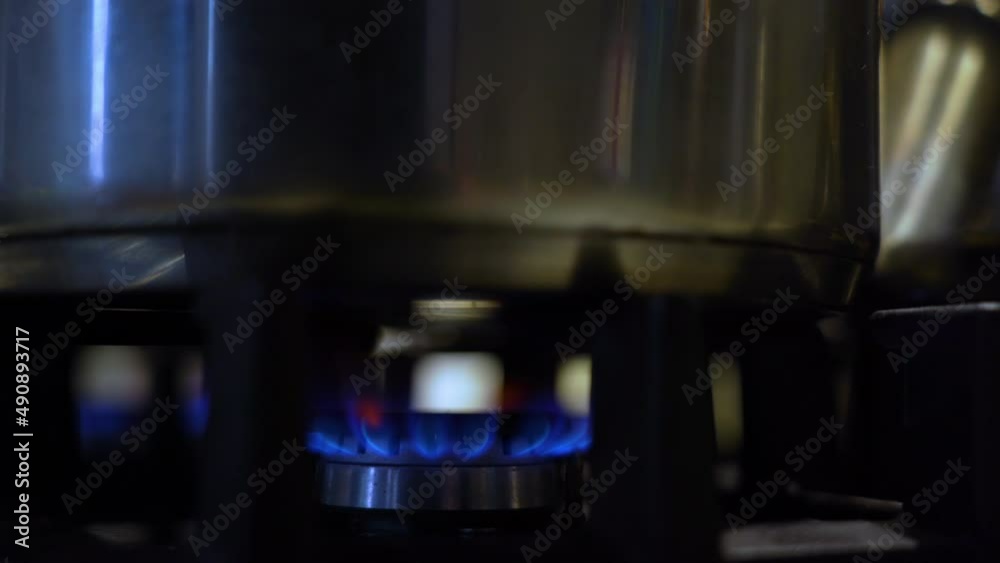 saucepan over a flame on a gas cooker. Close up view gas stove cooking food in metal pot at  kitchen with blue fire flame. Pot on modern gas cooktop in kitchen