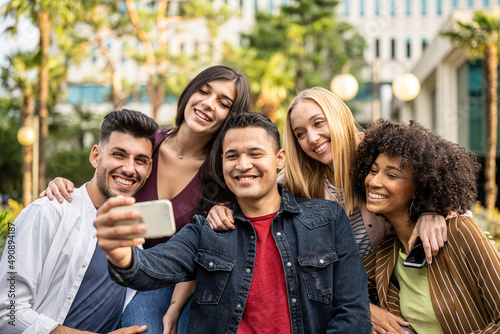 gen z people taking selfie with smartphone, five people group having fun outdoors, bonding friendship hangout