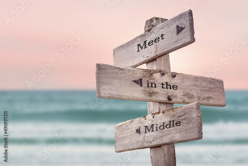meet in the middle text quote written on wooden signpost by the sea. Positive pink turqoise pastel theme.