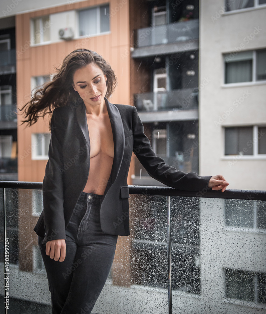 Gorgeous glamour brunette woman with black jacket posing on modern balcony with amazing view on city .Portrait of a Stylish fashionable woman with long legs , black jeans wearing in balcony