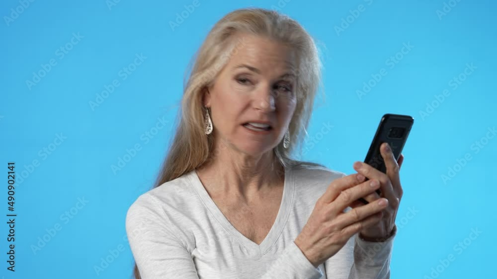 Portrait smiling mature woman talk on mobile cell phone conducting video chat happy conversation isolated on solid blue background studio Portrait smiling mature woman talk on mobile cell phone conducting video chat happy conversation isolated on solid blue background studio