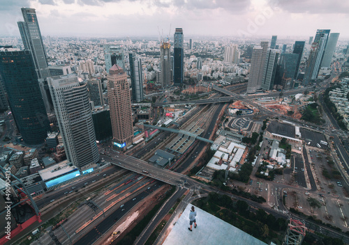 Young man roofer standing on the high roof of Tel Aviv with view of moders skyscrapers