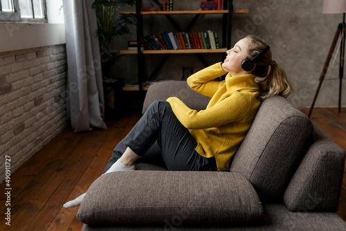 Beautiful pleased woman listening to music in headphones while sitting on sofa at home