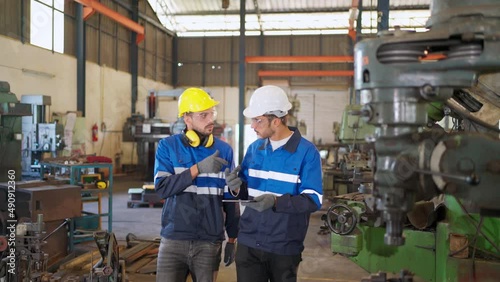 Engineer walking in the production line and discussing on the machine or equipment at factory. Wearing safety helmet and glasses to prevent accident. Industrial, maintenance and technology concept.