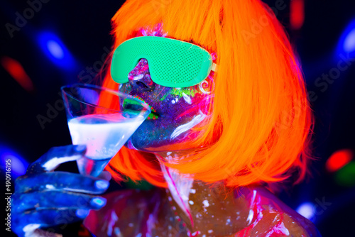 Fashion model woman drinking alcoholic cocktail in neon light, disco night club. Beautiful dancer model girl colorful bright fluorescent make-up