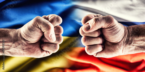 Confrontation of two fists against each other above the flags of Ukraine and Russia