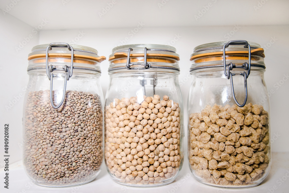 Tres tarros de cristal llenos con diferentes tipos de legumbres. Concepto de conservación de alimentos en la despensa. Bote de soja texturizada, lentejas y garbanzos. Tres tarros de cristal llenos con diferentes tipos de legumbres. Concepto de conservación de alimentos en la despensa. Bote de soja texturizada, lentejas y garbanzos.