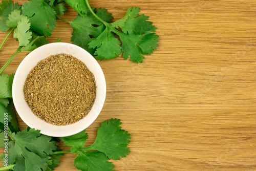 Ground coriander on the saucer and cilantro sprigs aroundon wooden textured background. Spice top view. photo