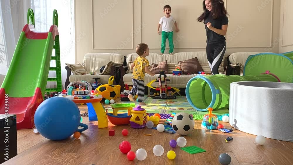 Mom and two children are dancing in the children's room among the scattered toys. A mess in the children's room. Children among scattered toys