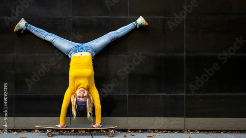 Athelic young woman upside down on a skateboard, black wall background, yellow shirt and blue jeans, generation z female crazy lifestyle photo