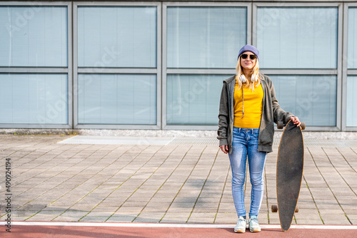 young happy and smiling girl with long board posing on a cycle, generation z fashionable woman living the city, minimal concept with copy space, yellow and blue palette © MandriaPix