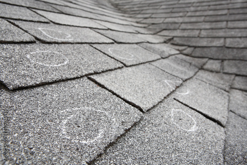 Old roof with hail damaged shingles, chalk circles mark the damage. Shallow depth of field