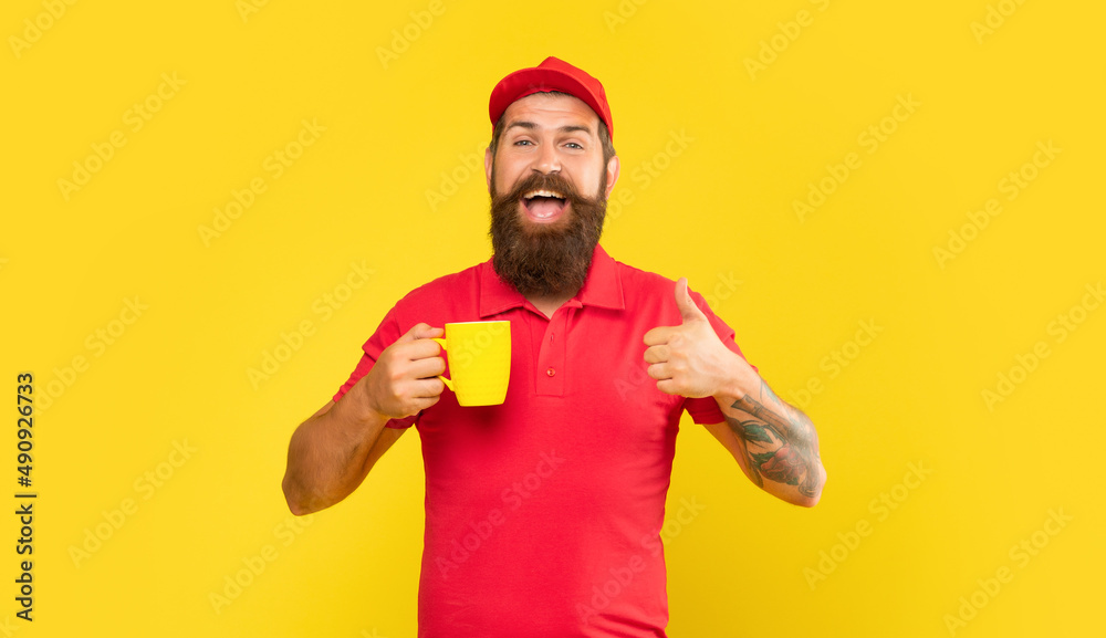Happy bearded man in casual red cap and tshirt giving thumb holding cup yellow background, coffee Happy bearded man in casual red cap and tshirt giving thumb holding cup yellow background, coffee