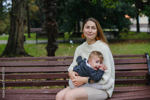 A girl with a small child is sitting walking in a park. Mom holds a baby in her arms and smiles.