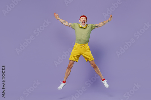 Full size body length sporty elderly gray-haired bearded man 40s years old in headband khaki t-shirt spreading hands in jump bounce isolated on plain pastel light purple background studio portrait