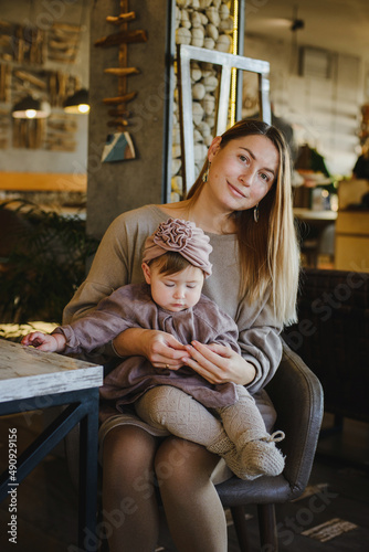 A young girl with a small child is sitting on a chair in a cafe. Mom holds a baby in her arms and looks at the camera